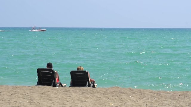 Young Couple Lying On A Lounge Chair On The Beach Watching