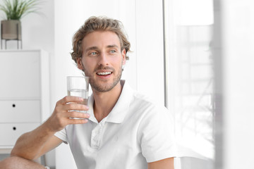 Young man holding glass of clean water indoors