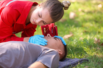 Woman in uniform checking for breathing of unconscious man outdoors. First aid