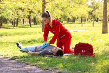 Woman in uniform performing CPR on unconscious man outdoors. First aid
