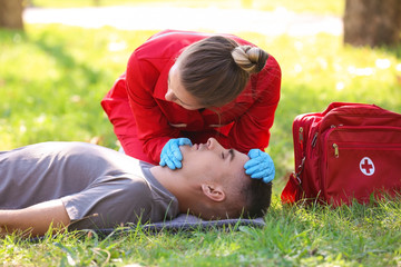 Woman in uniform checking for breathing of unconscious man outdoors. First aid
