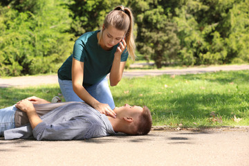 Passerby calling ambulance while checking pulse of unconscious man outdoors. First aid