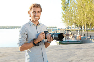 Handsome male photographer holding professional camera at pier. Space for text