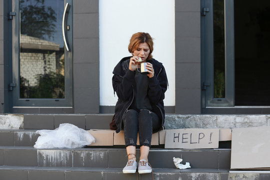 Poor woman with piece of bread and mug on city street