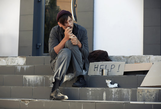 Poor homeless man eating piece of bread on city street