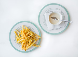 Fried French fries on a plate with sauce on a white table.