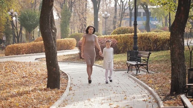 Mom and daughter are walking along an avenue strewn with autumn yellow foliage. Happy family on a walk in the city park