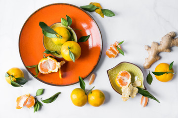 Still life in the style of flatlay. Ripe juicy tangerines against the background of an orange plate and a white background, with green foliage and ginger root.