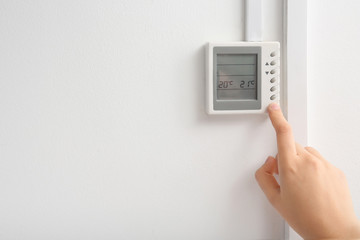 Woman adjusting thermostat on white wall, closeup. Heating system