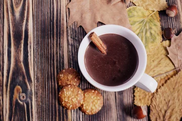 Fotobehang Hot chocolate with cinnamon stick in cup leaves nuts cookies on wooden table Autumn hot drink Autumn concept Top view © Maria Volkova