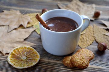 Hot chocolate with cinnamon stick in cup leaves nuts cookies dried oranges on wooden table Autumn hot drink Autumn concept
