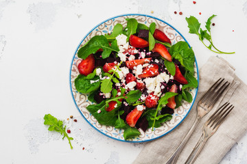 Beets, strawberries, feta cheese and arugula salad in ceramic plate on old concrete table background. Top view.