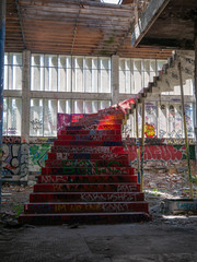 Stairs leading up to another floor in an old abandoned building or factory, completely destroyed and vandalized, painted with colourful graffiti street art