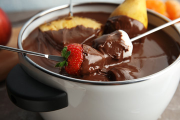 Dipping fresh fruits into pot with tasty chocolate fondue, closeup