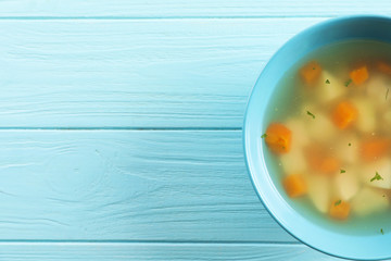 Bowl of fresh homemade soup to cure flu on wooden background, top view with space for text