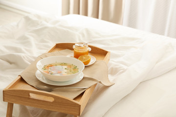 Tray with bowl of fresh homemade soup to cure flu on bed