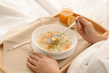 Obraz na płótnie Canvas Sick woman eating fresh homemade soup to cure flu in bed at home, closeup