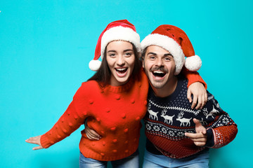 Fototapeta premium Young couple in warm sweaters and Christmas hats on color background