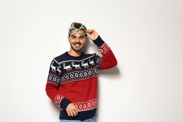 Young man in Christmas sweater with party glasses on white background
