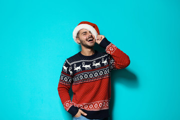 Young man in Christmas sweater and hat on color background