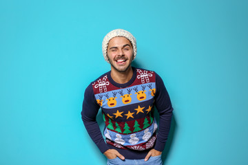 Young man in Christmas sweater and knitted hat on color background