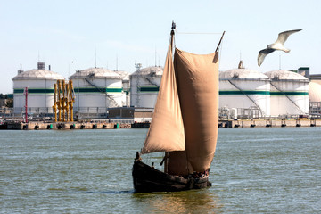 An ancient boat with sails on the background of a port oil terminal © Juozas55