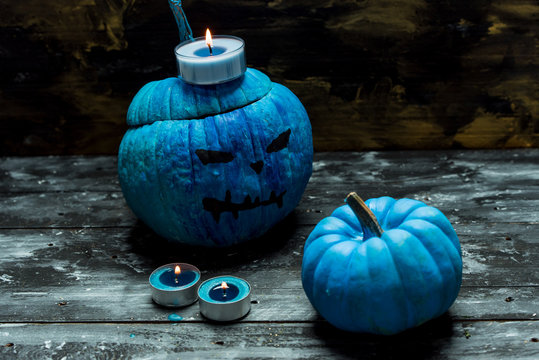 horribly blue Halloween, painted blue pumpkins on a dark, rustic background, next to lit candles