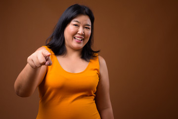 Beautiful overweight Asian woman smiling and pointing finger at camera