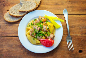Served lunch or dinner – stewed potato with meat and cut green onion on a plate and bread with sunflower seeds on the table.