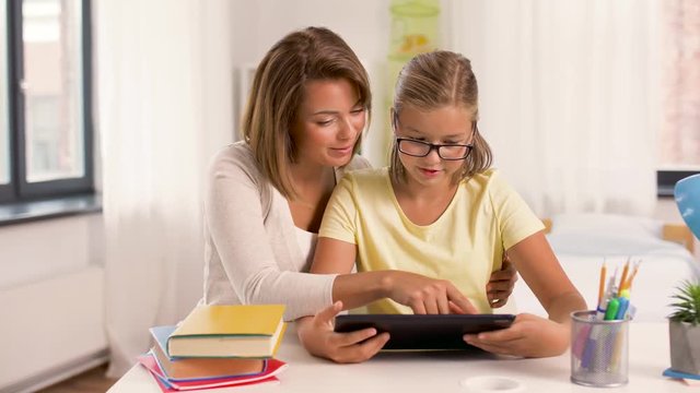 education, family and learning concept - mother and daughter with tablet pc computer doing homework together at home