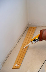 worker applies glue on wooden skirting board for wall mounting