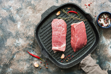 Raw beef steak with spices and herbs on a grill pan, rustic background, top view.