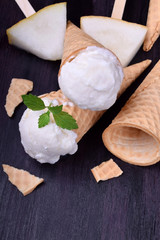 White ice cream in waffle cones. Pieces of melon around on a dark table