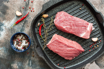 Fresh raw beef meat in a grill pan. Two pieces of beef with spices for cooking. View from above,Overhead
