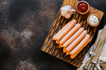 Raw sausages with garlic and sauces on wooden board on dark concrete background. Top view.