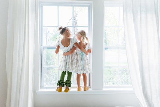 Two girls standing on a window sill