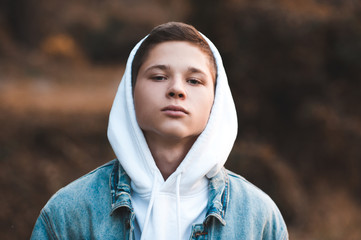 Teen boy 16-17 year old wearing white hoodie and denim jacket closeup. Looking at camera. 20s.