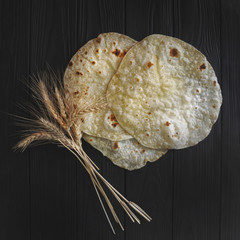 Pita bread three pieces and ripe ears of wheat on a dark wooden table.