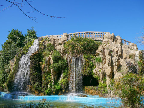 Artificial waterfall with a bridge over stone in the park Parque Genov&eacute;s in C&aacute;diz, Spain