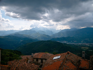 Fototapeta na wymiar Landscape of dark clouds over foggy green hills in rural Tuscany, Italy, over the orange rooftop of a small village