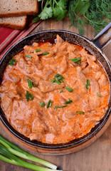 Pieces of meat stewed in tomato and sour cream sauce in the frying pan