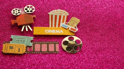 tub of popcorn with cinema sign and 3d glasses movie tickets on film strip movie projector and reel on dark pink shiny background