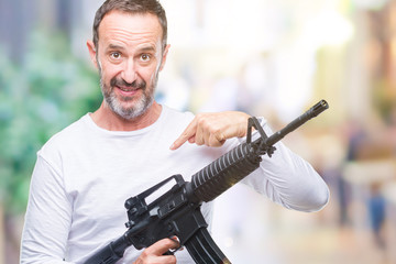 Middle age senior hoary criminal man holding gun weapon over isolated background with surprise face pointing finger to himself