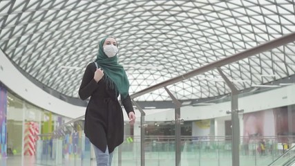 Pretty muslim woman in a hijab with a backpack and a medical mask on her face goes shopping,slow mo