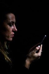 Young girl at night looking into her smartphone isolated on black background