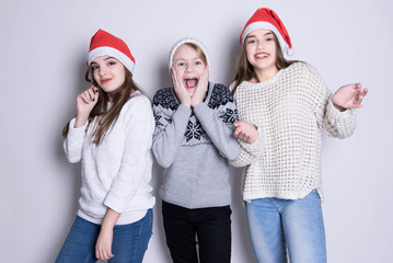 Portrait of three happy teenagers in santa claus hat and white warm sweaters. Merry Christmas and Happy Holidays concept. Family holiday, party over white background. Xmas.