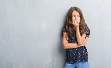 Young hispanic kid over grunge grey wall looking stressed and nervous with hands on mouth biting...