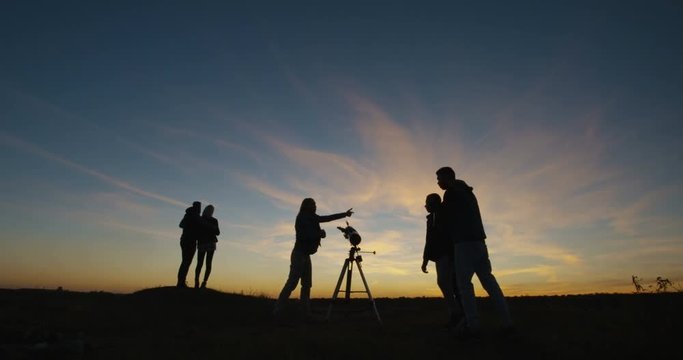 Medium shot of friends stargazing together and using a professional telescope at night near a stream