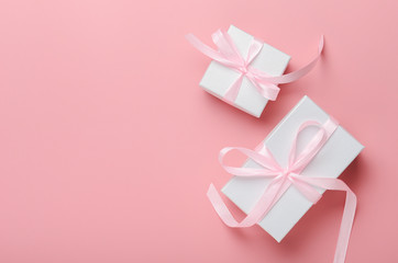 White gift box on a pink background with a pink ribbon. A birthday present, women's day or Christmas. Top view, save space, flat lay