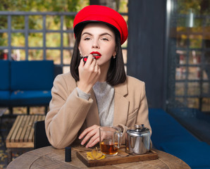Beautiful young brunette in a red hat painting her lips with red lipstick